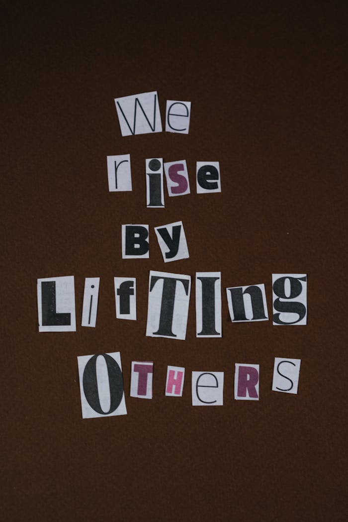 Inspirational cutout text 'We rise by lifting others' on brown backdrop.